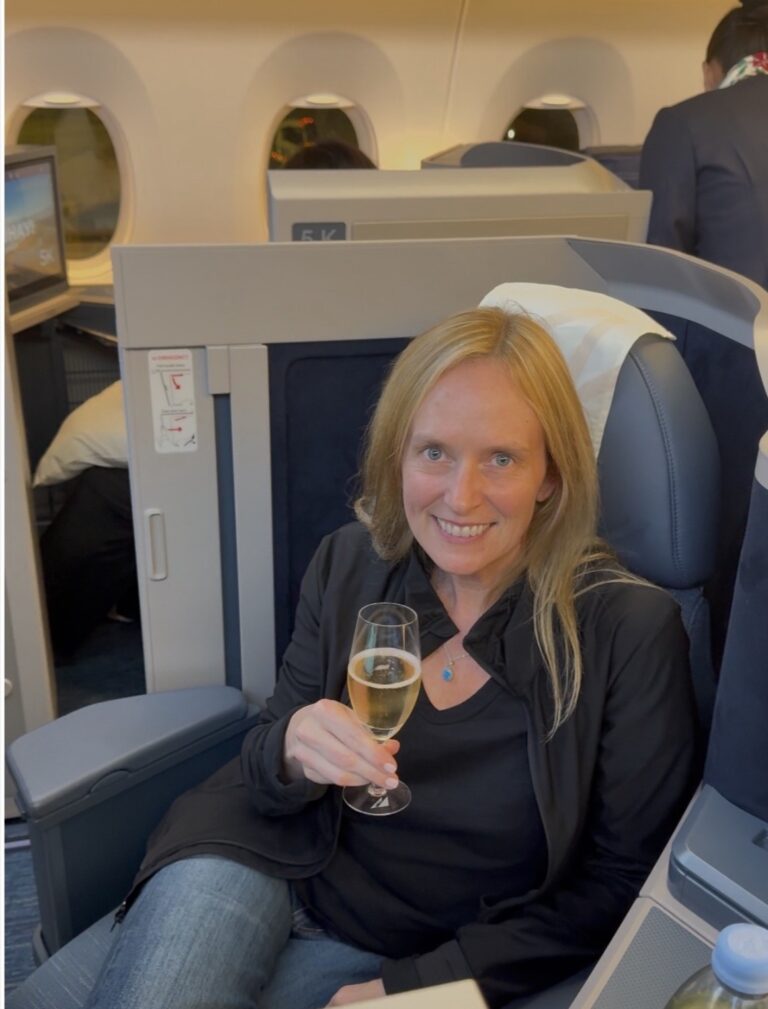 Lisa raising a glass of champagne in her seat on a plane