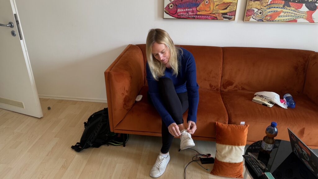 Lisa sitting on an orange couch lacing up a white travel sneaker