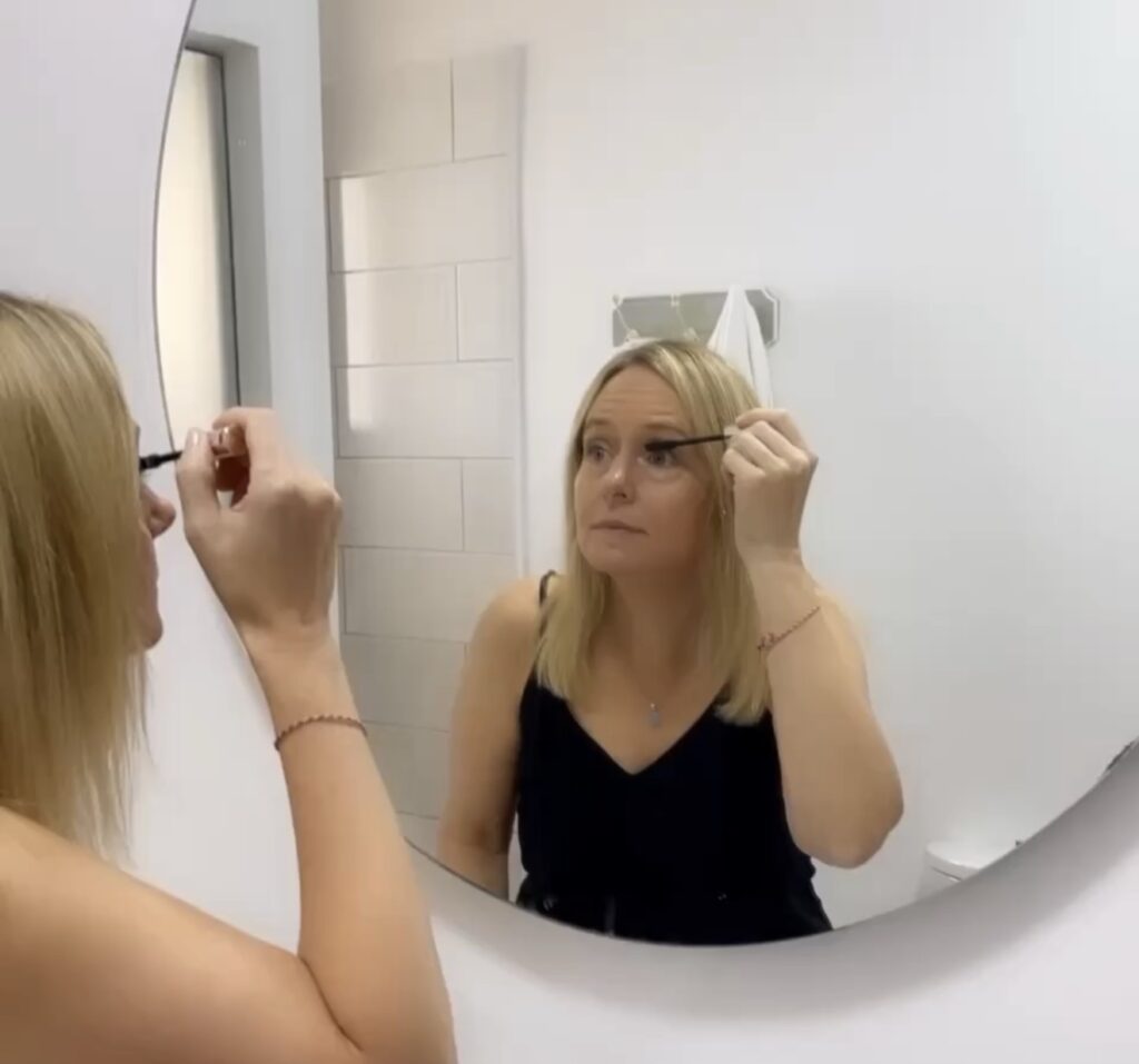 Lisa applying mascara at a bathroom mirror