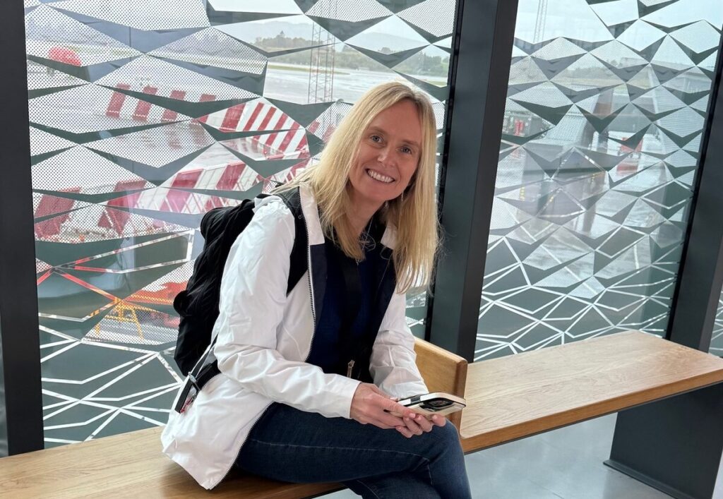 Lisa sitting in an airport waiting area, smiling at the camera