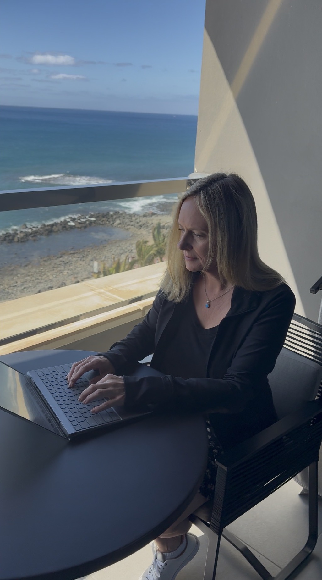 Lisa Reidmiller working on a laptop on a balcony above the sea